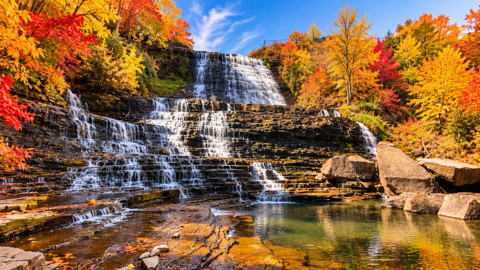 Hamilton waterfall cascading over limestone escarpment surrounded by autumn foliage in orange and red